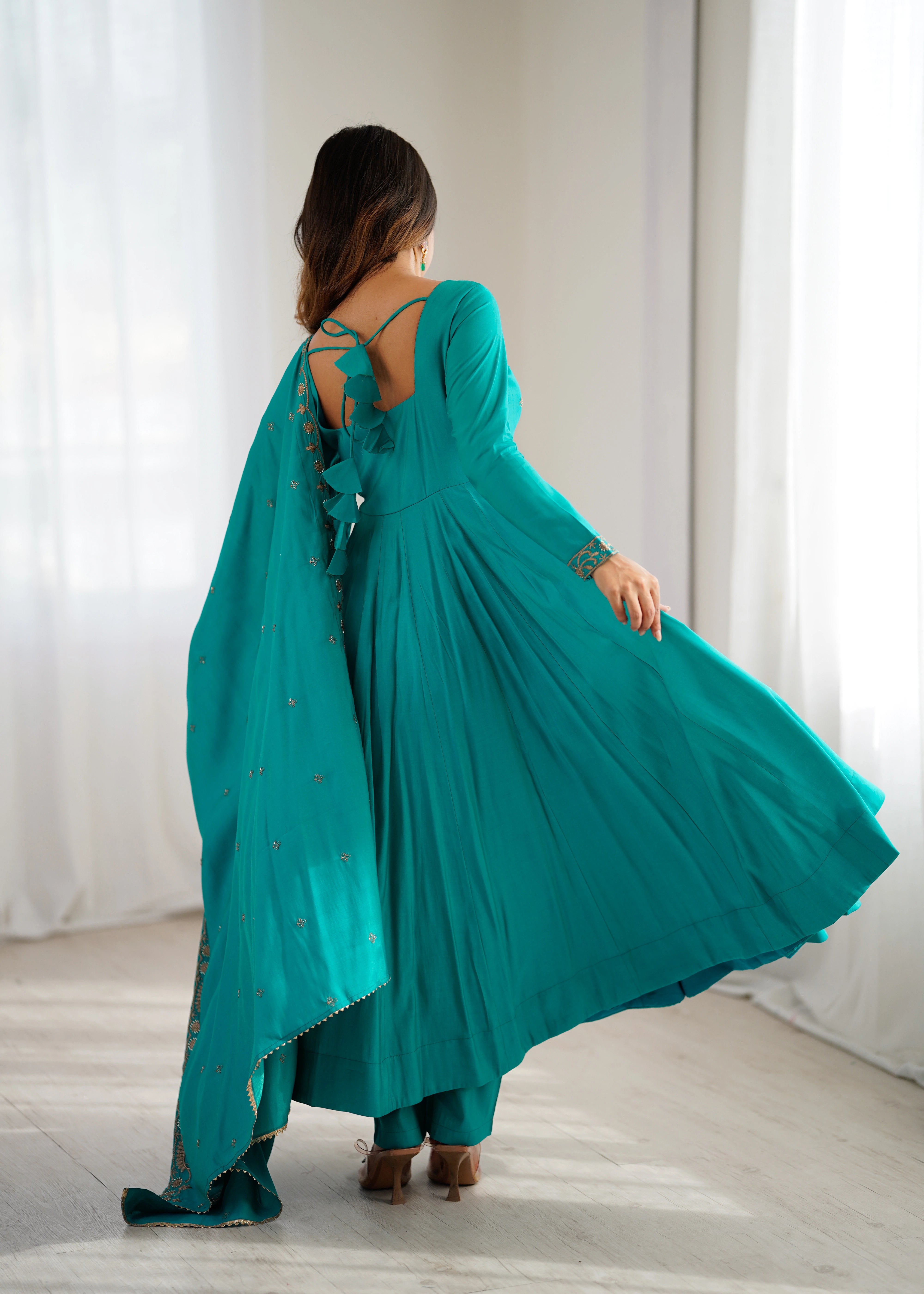 Woman in a teal dress with a backless design, standing in a room with white curtains.